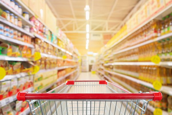 Empty red shopping cart with supermarket aisle with seasoning and cooking vegetable oil bottles product shelves interior defocused blur background